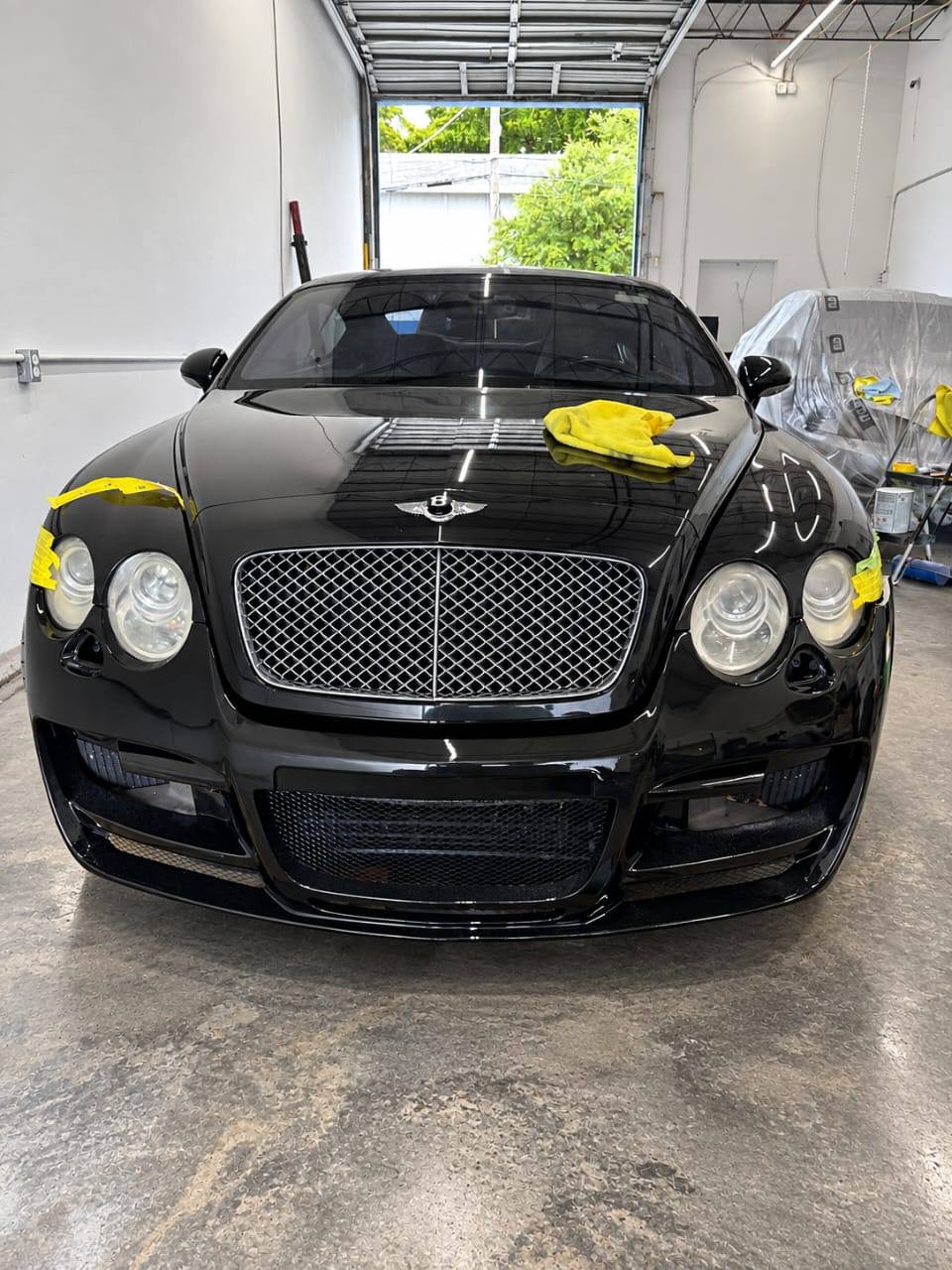 Black Bentley Continental GT taped and prepped for refinishing inside the shop — Total Care Collision Pompano Beach FL