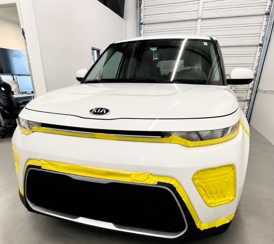 Front bumper of a white Kia Soul masked with yellow tape for paint — Total Care Collision Pompano Beach FL