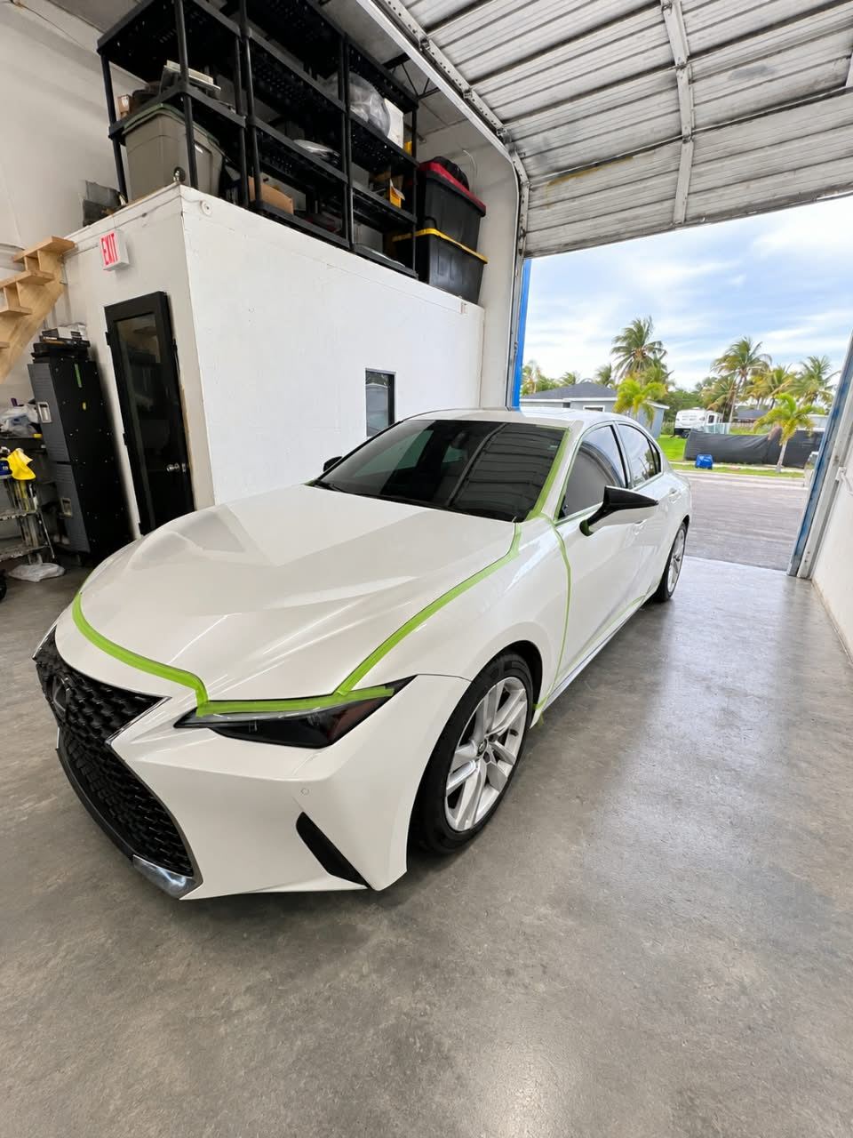 White Lexus IS taped for refinishing at the shop door, palm trees outside — Total Care Collision Pompano Beach FL