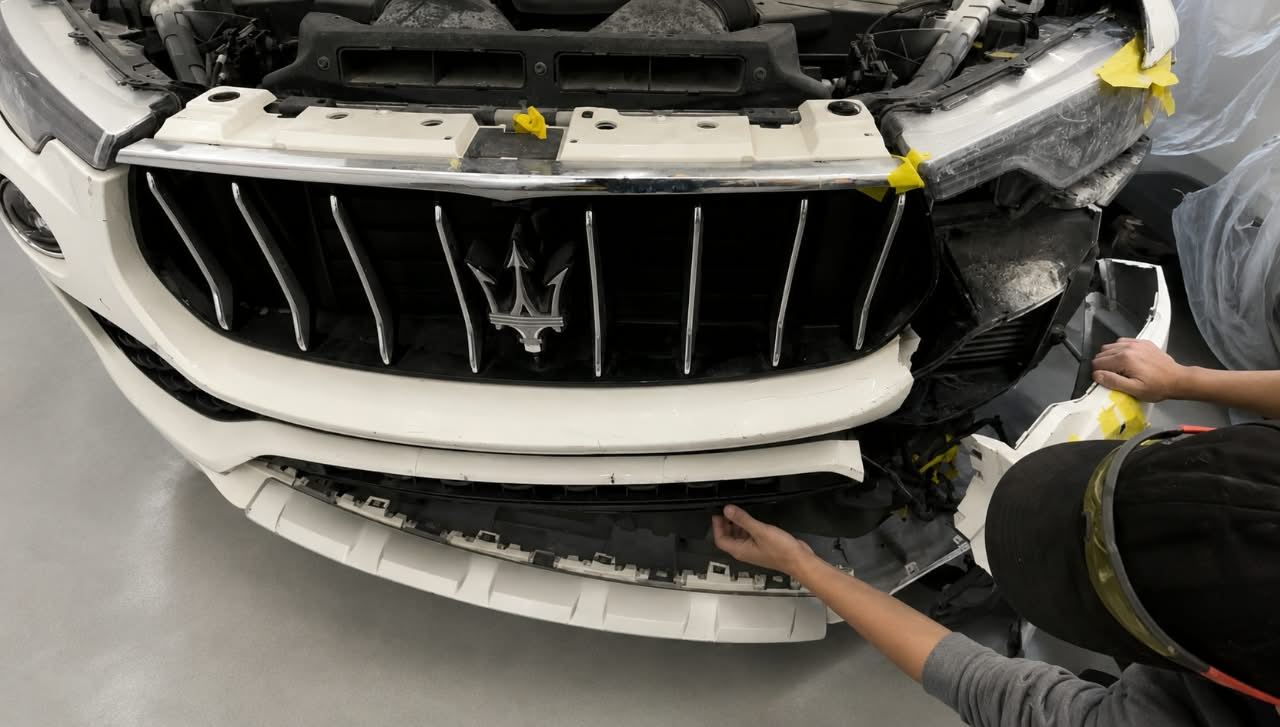 Technician’s hands fitting the front bumper and grille on a white Maserati Levante — Total Care Collision Pompano Beach FL