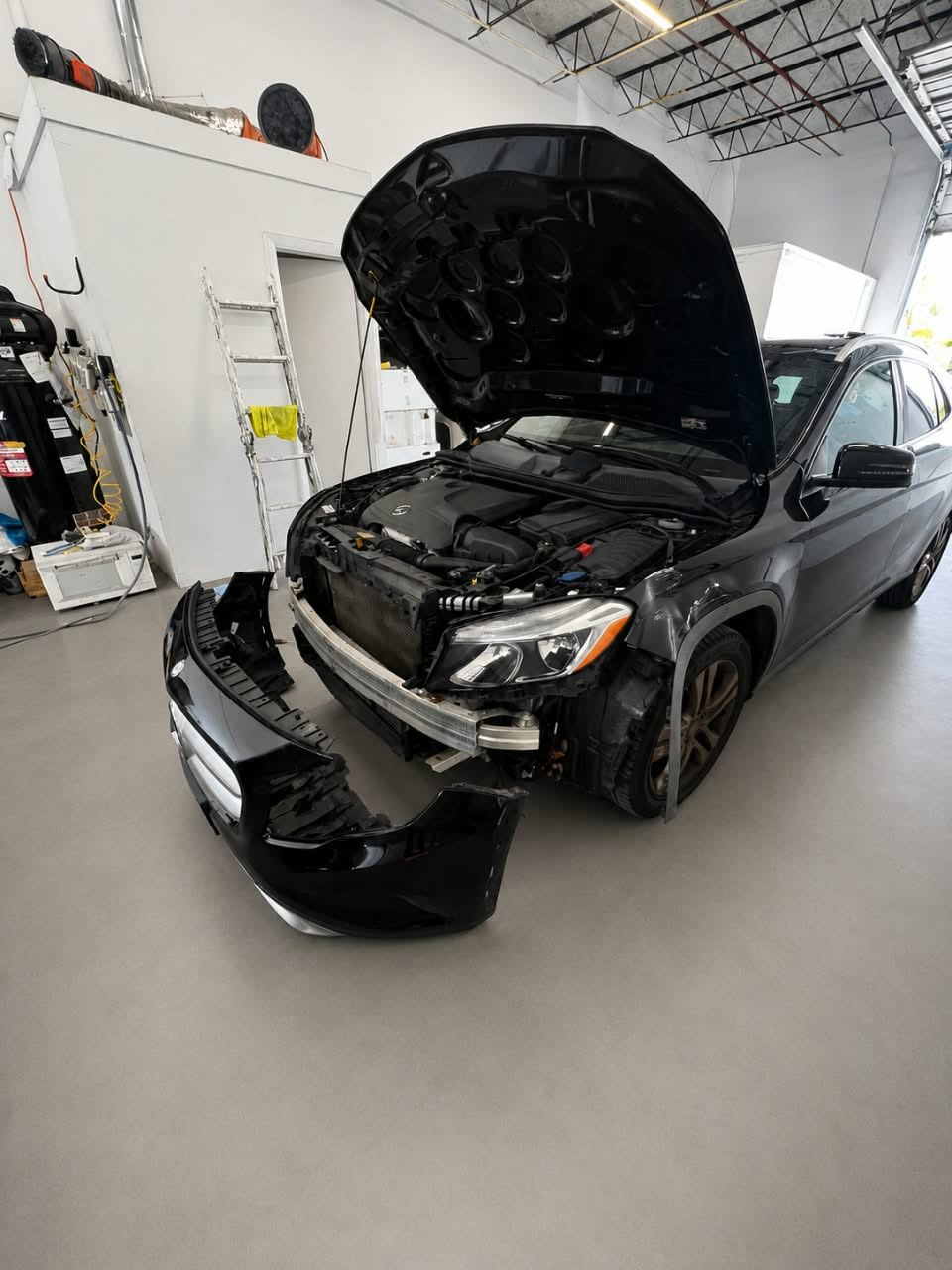 Dark Mercedes GLA with the front bumper removed and hood open for collision repair — Total Care Collision Pompano Beach FL