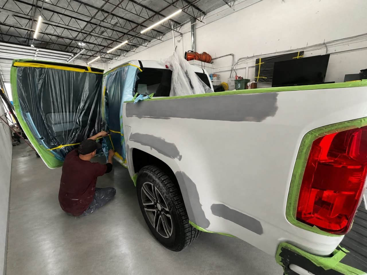 Technician masking a white pickup truck with primer spots for paint — Total Care Collision Pompano Beach FL