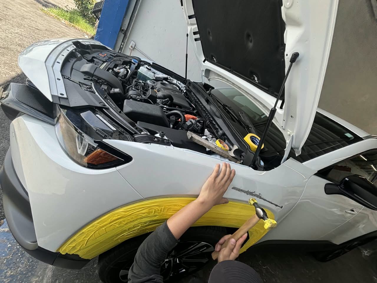 Technician’s hands with a body hammer repairing the fender of a white Toyota — Total Care Collision Pompano Beach FL